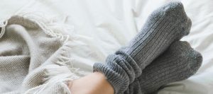Feet crossed with gray socks on bed under blanket