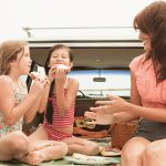 Mother and daughters eating sandwiches on car boot