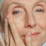 Portrait of Beautiful Senior Woman Gently Applying Under Eye Face Cream. Elderly Lady Makes Her Skin Soft, Smooth, Wrinkle Free with Natural anti-aging Cosmetics. Product for Beauty Skincare, Makeup