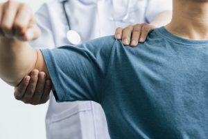A man with shoulder pain goes to the doctor, The doctor diagnoses the patient’s arm pain and shoulder pain. Concept of physical therapy and rehabilitation.