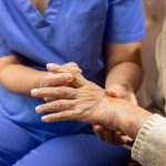 Caregiver massaging finger of elderly woman in painful swollen gout .