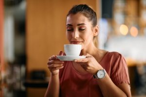 Young woman enjoying in smell of fresh coffee in a cafe.