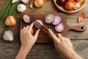 Woman cutting red onion on board at wooden table, top view