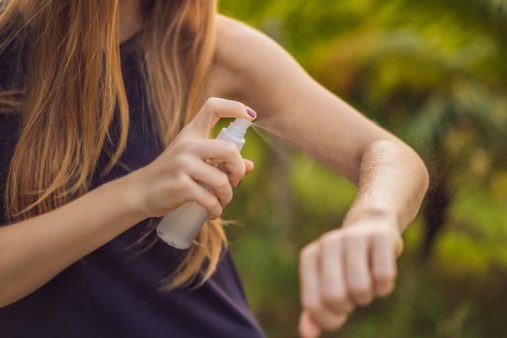 Woman spraying insect repellent on skin outdoor