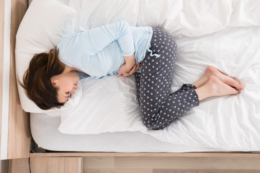 Mujer con dolor de estómago tumbada en la cama